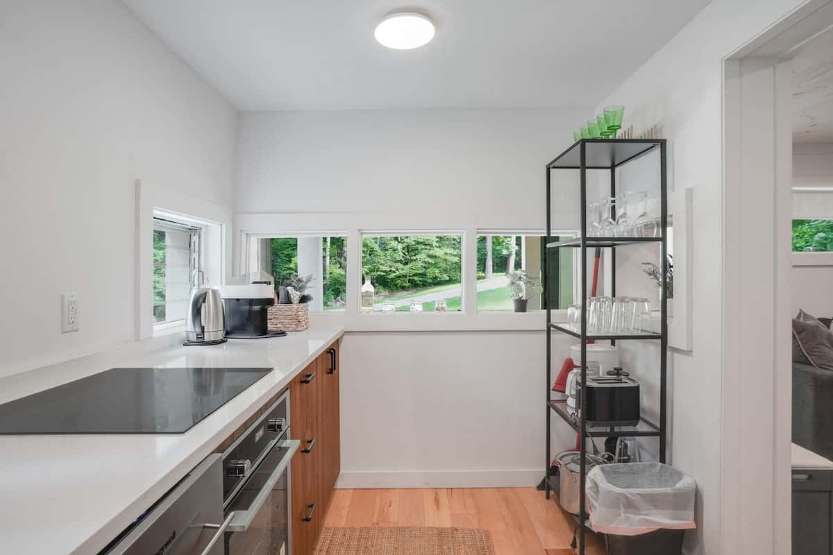 The kitchen run with its window over the sink and a black metal shelf unit at the end