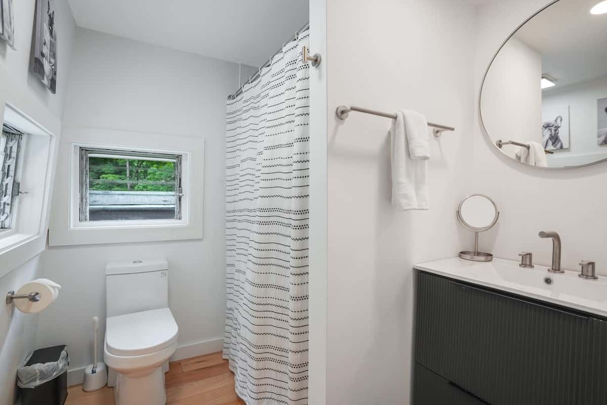 The full bathroom: shower with a curtain, toilet, vanity, and a small window