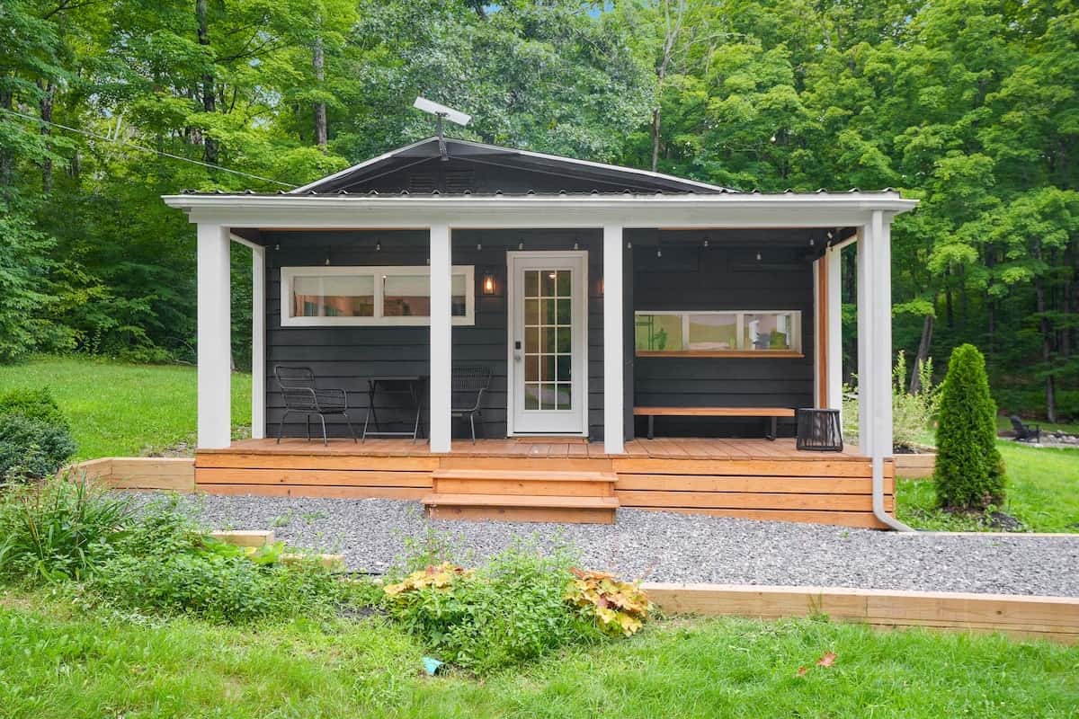 Front elevation of the cabin with its covered porch, cedar steps, and planting beds set in crushed stone