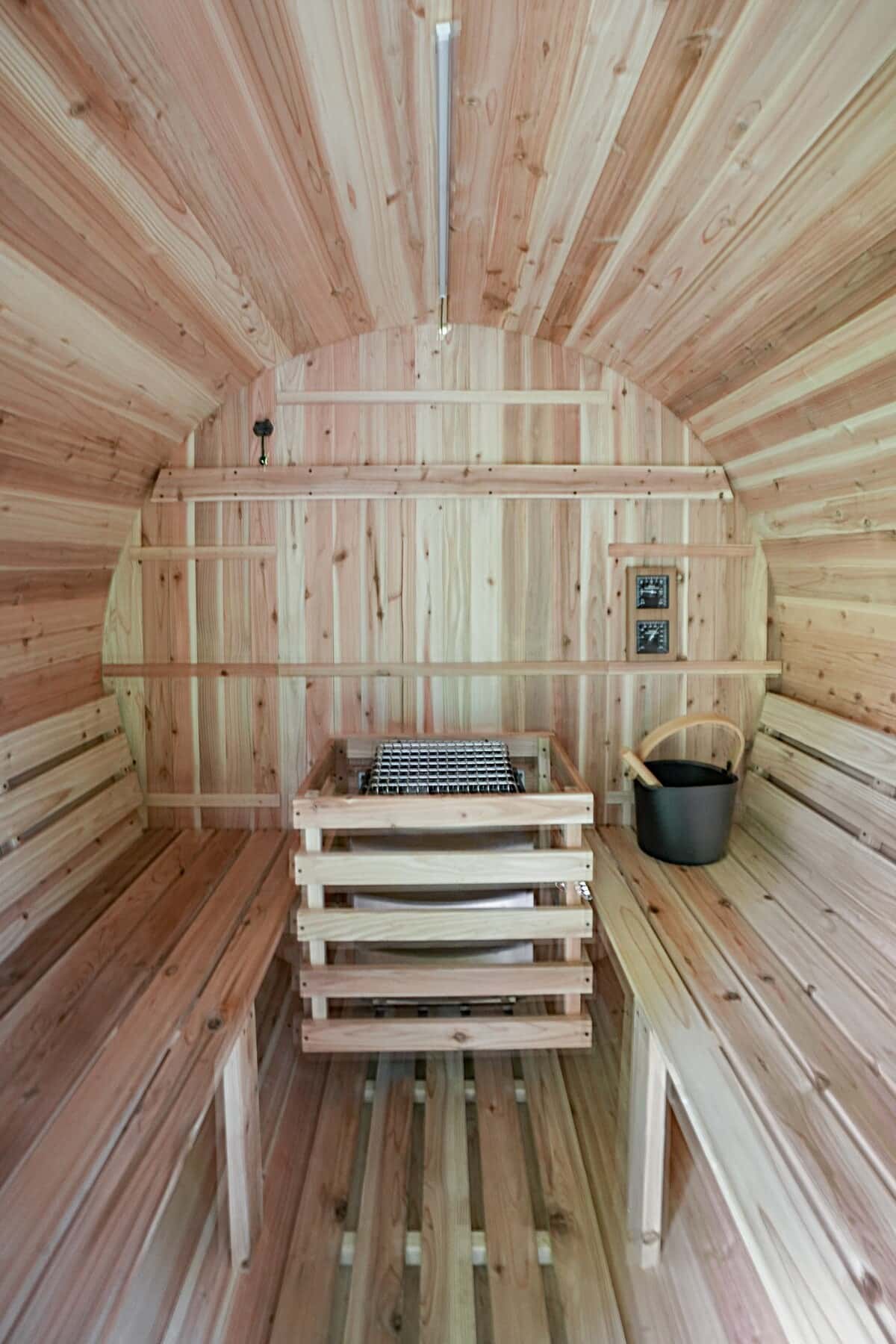 Inside the sauna: pale cedar benches and walls, a bucket and ladle on the lower bench